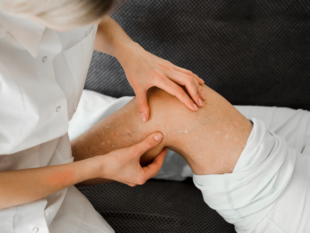 Healthcare professional gently examines a patient’s knee, checking the joint and surrounding skin during a calm clinical assessment.