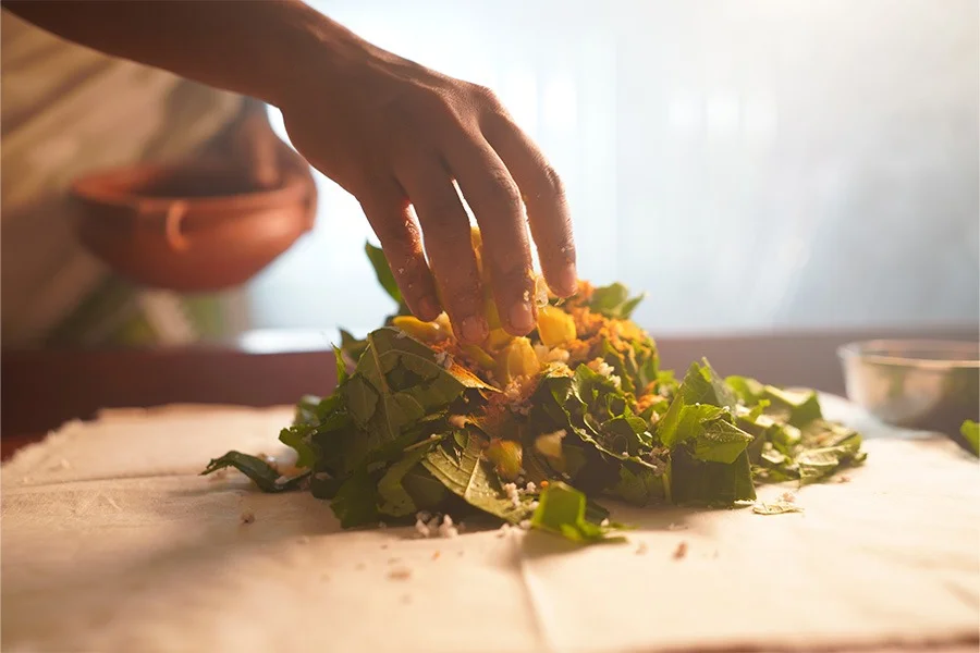 Hands gently arrange fresh herbs and vegetables into a rustic salad on a wooden board, bathed in warm sunlight in a cozy kitchen.