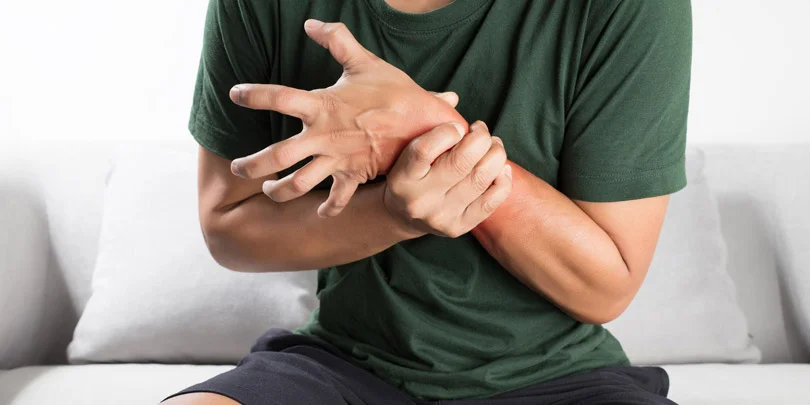 Seated person in a dark green shirt cradles a painful, reddened wrist and hand, suggesting discomfort or possible repetitive strain injury.