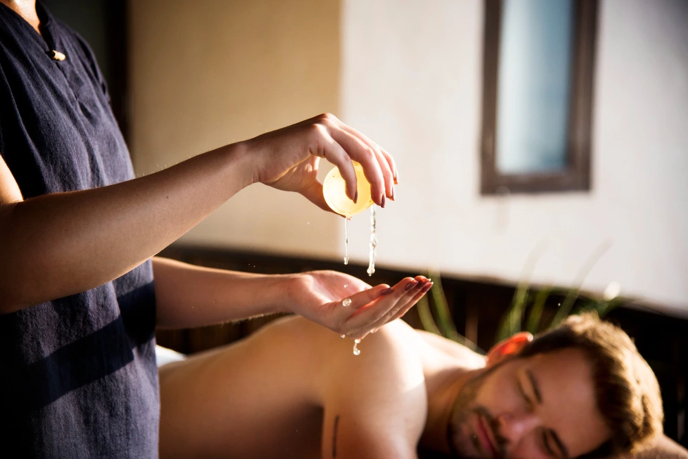 At a tranquil spa, a therapist drips massage oil onto a reclining man’s back during a soothing treatment, creating a calm, intimate mood.